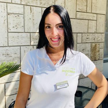 Giorgia works at Hotel Ausonia in Rimini, wearing a white polo with the hotel logo.
